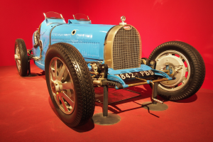 Ein blaues Rennauto auf einem Podest vor einem roten Hintergrund in einem Museum.