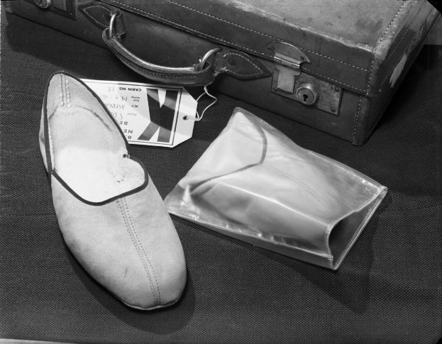 Ein Paar schwarze und weiße Schuhe mit einem Etikett, das neben einem Koffer auf einem Tisch liegt.